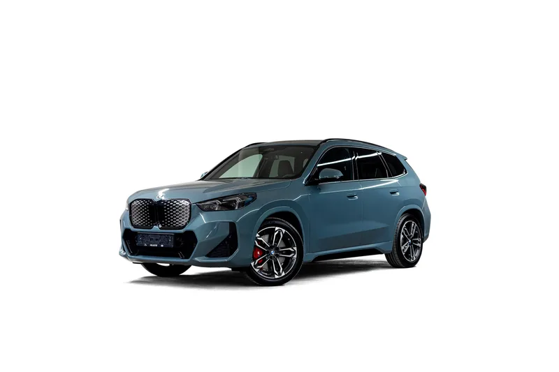 Blågrå BMW iX1 fotografert skrått forfra på hvit bakgrunn
