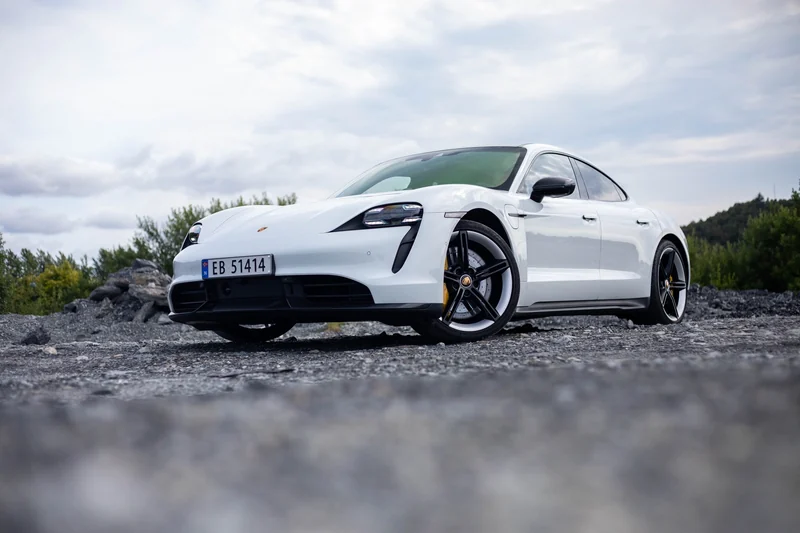Hvit Porsche Taycan fotografert på grus ved sjøen