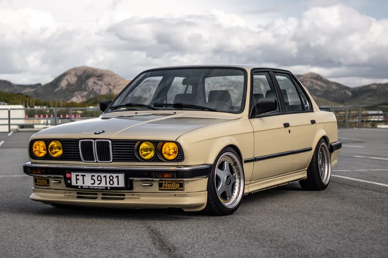 Beige klassisk BMW E30 på parkeringsdekk med fjell i bakgrunnen