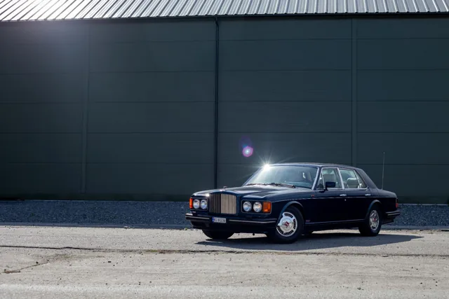 Mørkeblå klassisk Bentley fotografert mot en grønn vegg