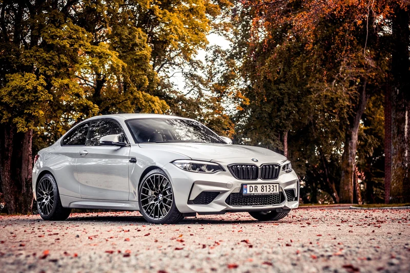 Hvit BMW M2 fotografert blant høstfargede trær