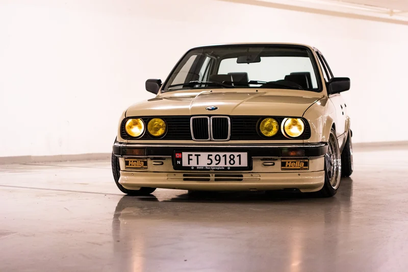 Gullfarget klassisk BMW E30 fotografert mot lys bakgrunn